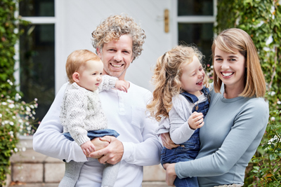 family posing together with two young children smiling on a porch surrounded by greenery capturing joyful moments of five beautiful smiles